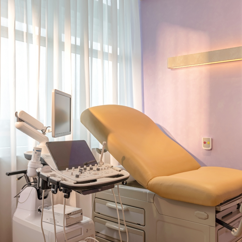 Ultrasound machine beside an adjustable examination bed in a bright GenPrime Fertility treatment room.
