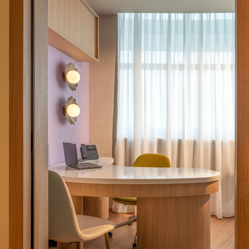 GenPrime Fertility consultation room with a curved desk, visitor chairs, laptop, warm wall lighting, and floor-to-ceiling curtains.