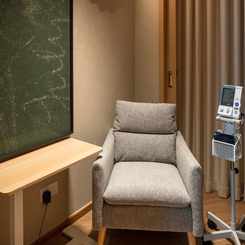 GenPrime Fertility consultation room with a grey armchair, wooden side table, privacy curtains, and a patient monitoring device.