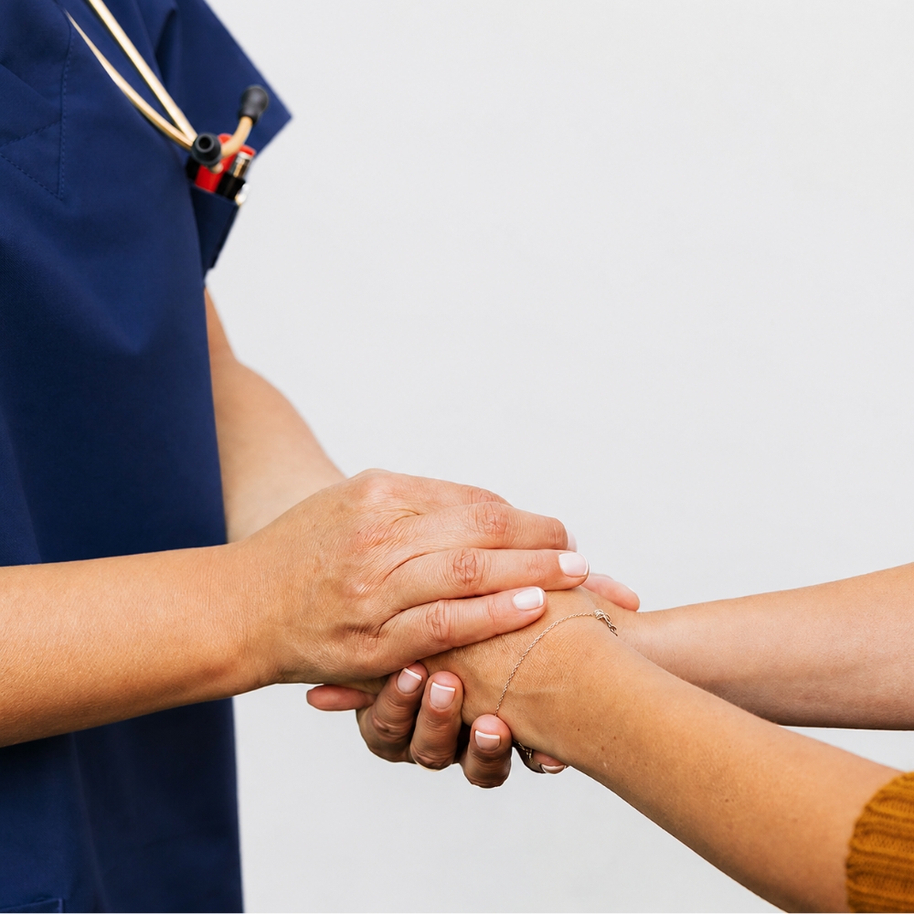 Healthcare professional in navy scrubs holding a patient’s hands in a supportive gesture.