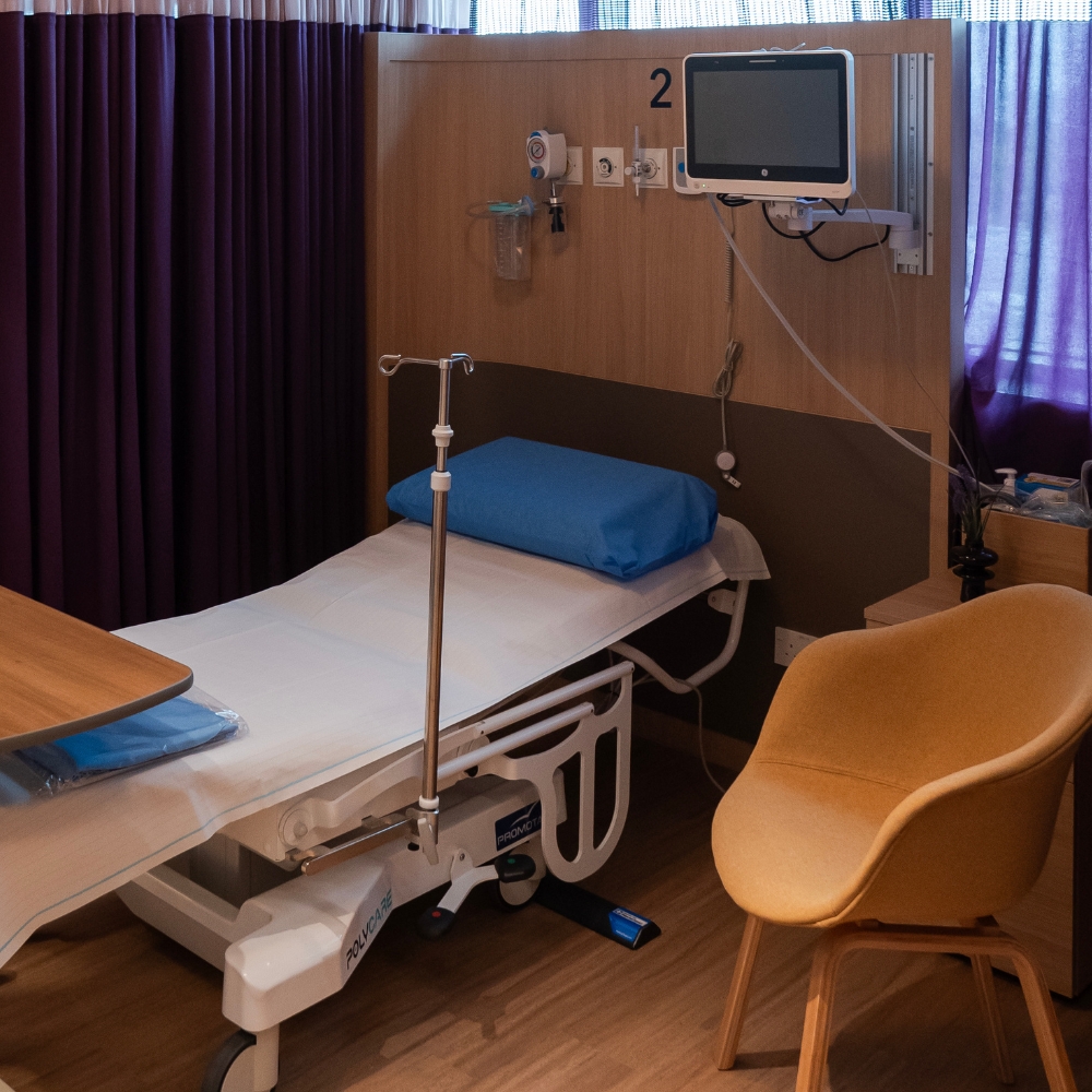 GenPrime Fertility treatment room with an adjustable medical bed, IV stand, patient monitor, privacy curtains, and a visitor chair.