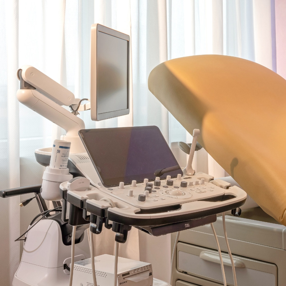 Ultrasound machine positioned beside an examination bed in a bright fertility clinic treatment room.