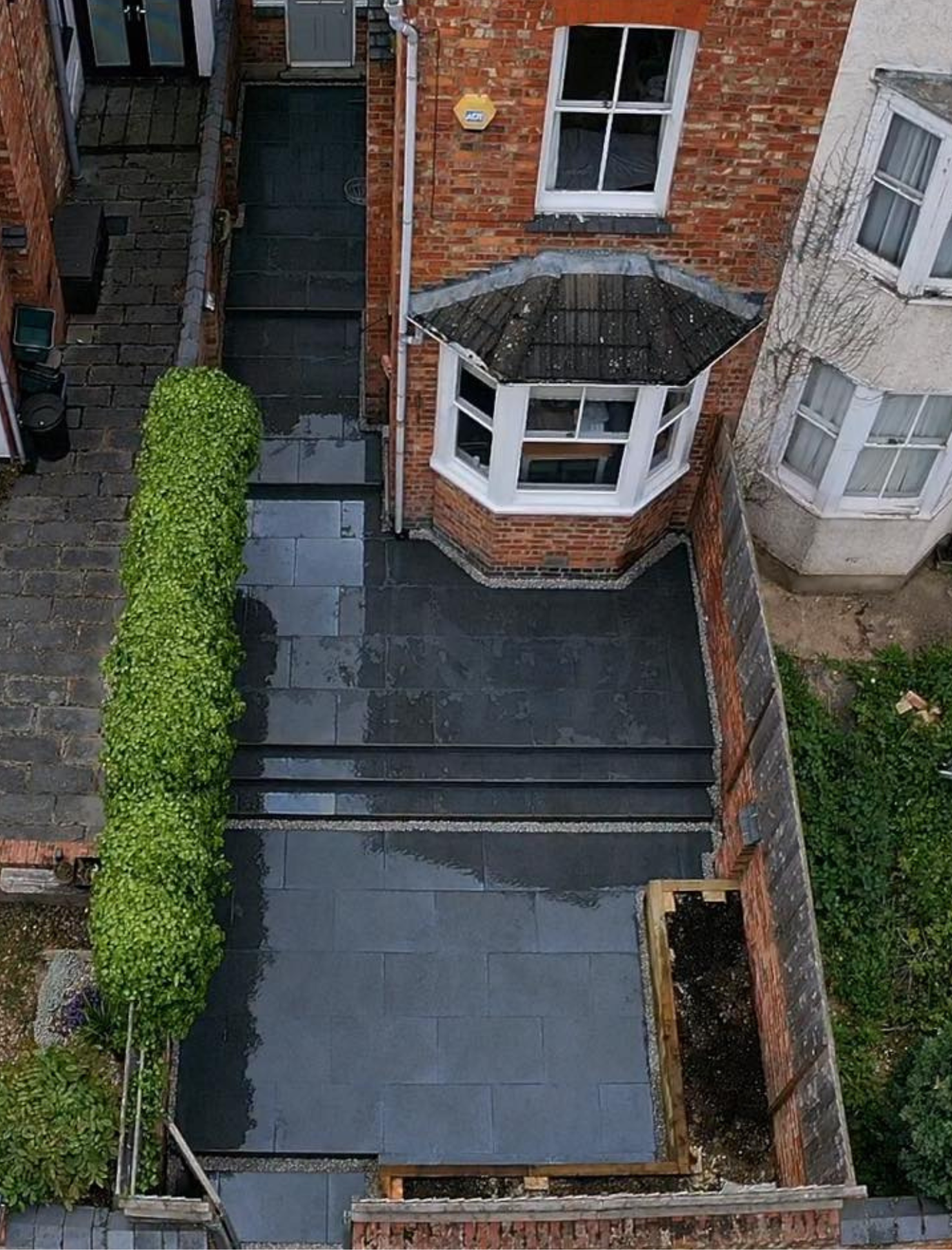 Aerial view of a newly completed patio and landscaping project beside a red brick home in Northamptonshire, showcasing clean paving, raised beds, and professional craftsmanship by Link Construction and Landscaping.
