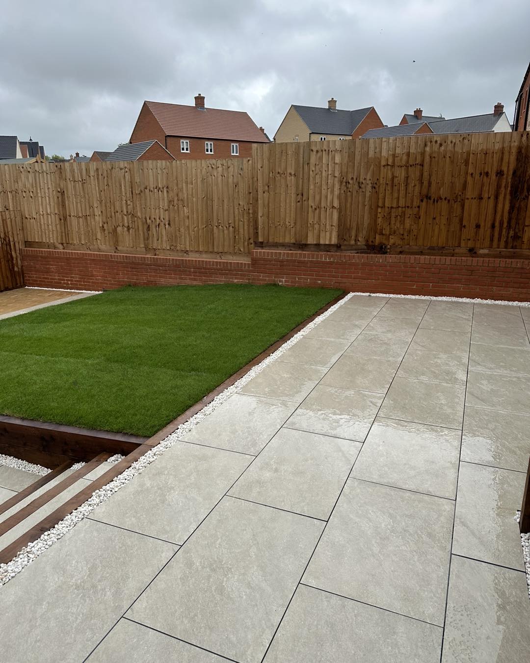 Modern Wellingborough garden featuring porcelain tile patio, fresh turf lawn, and wooden raised border with gravel edging.