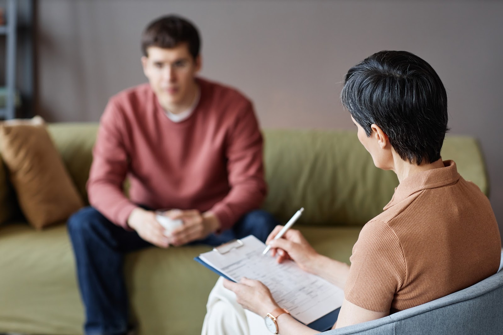 Psychologist writing notes while she meets with a male client