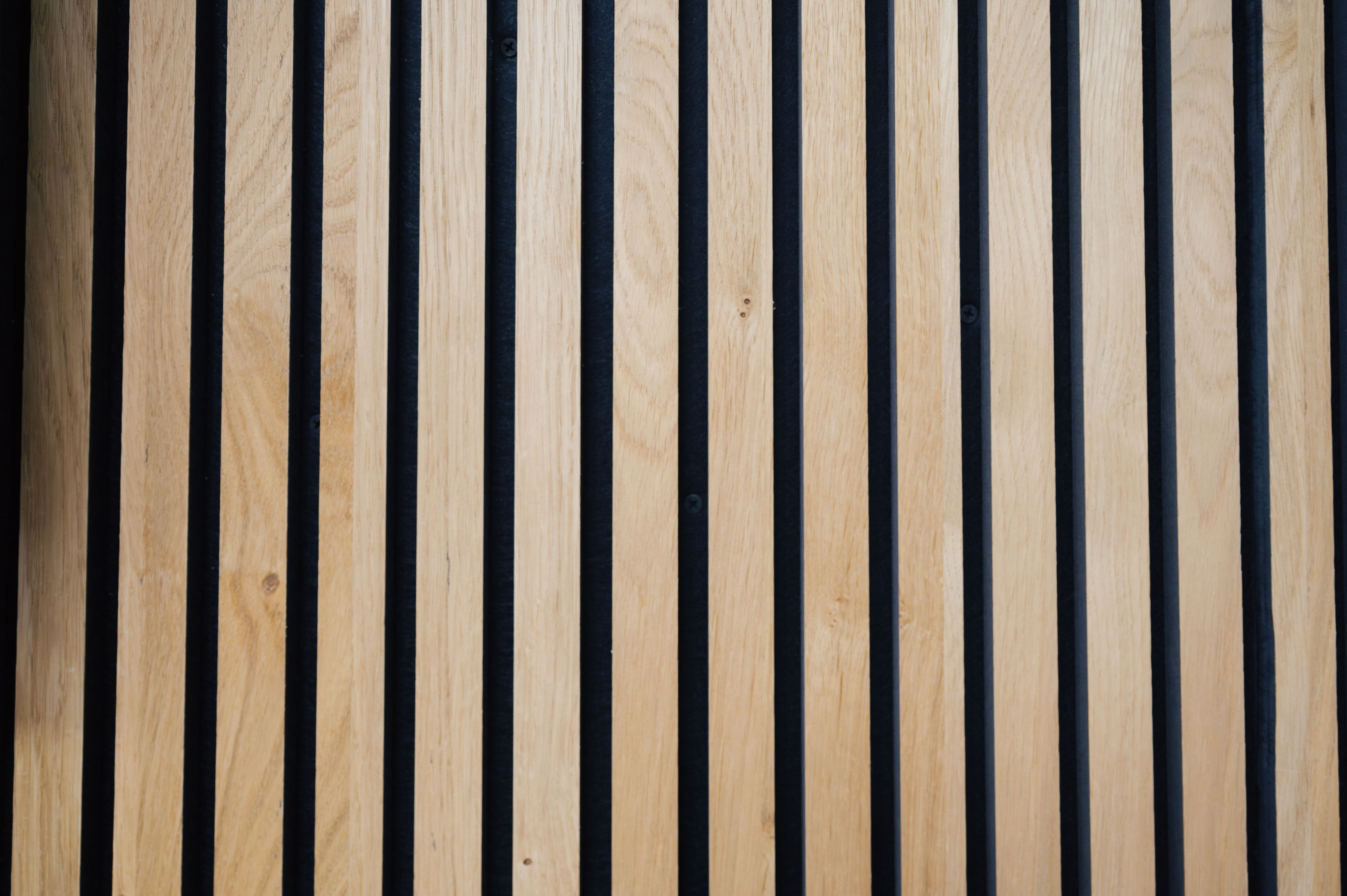 Vertical wooden slats with evenly spaced black gaps between them, forming a geometric pattern reminiscent of a dentist’s precise attention to detail.