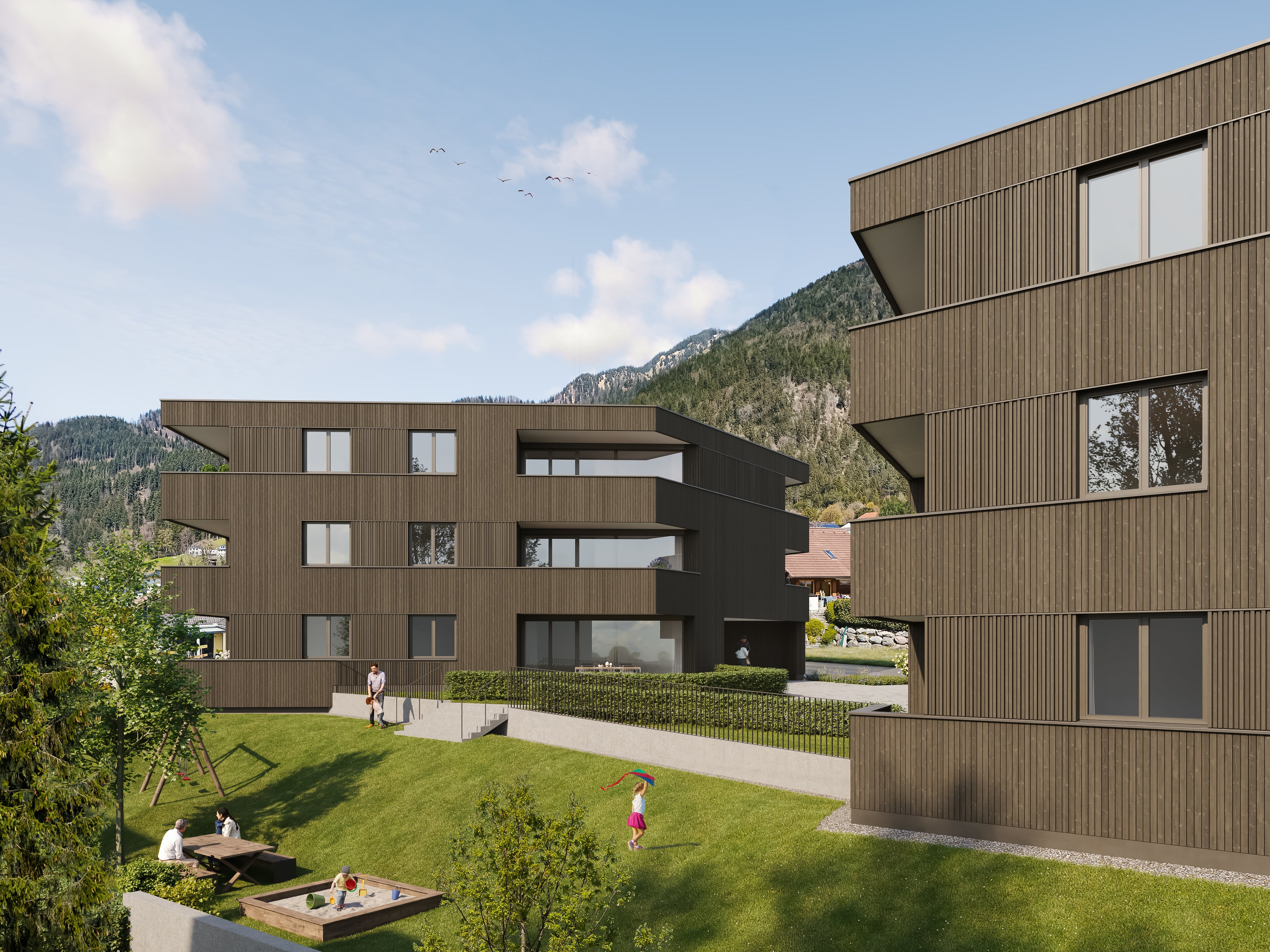 Modern brown apartment buildings with green lawn, people sitting, child flying kite, and mountains in background.