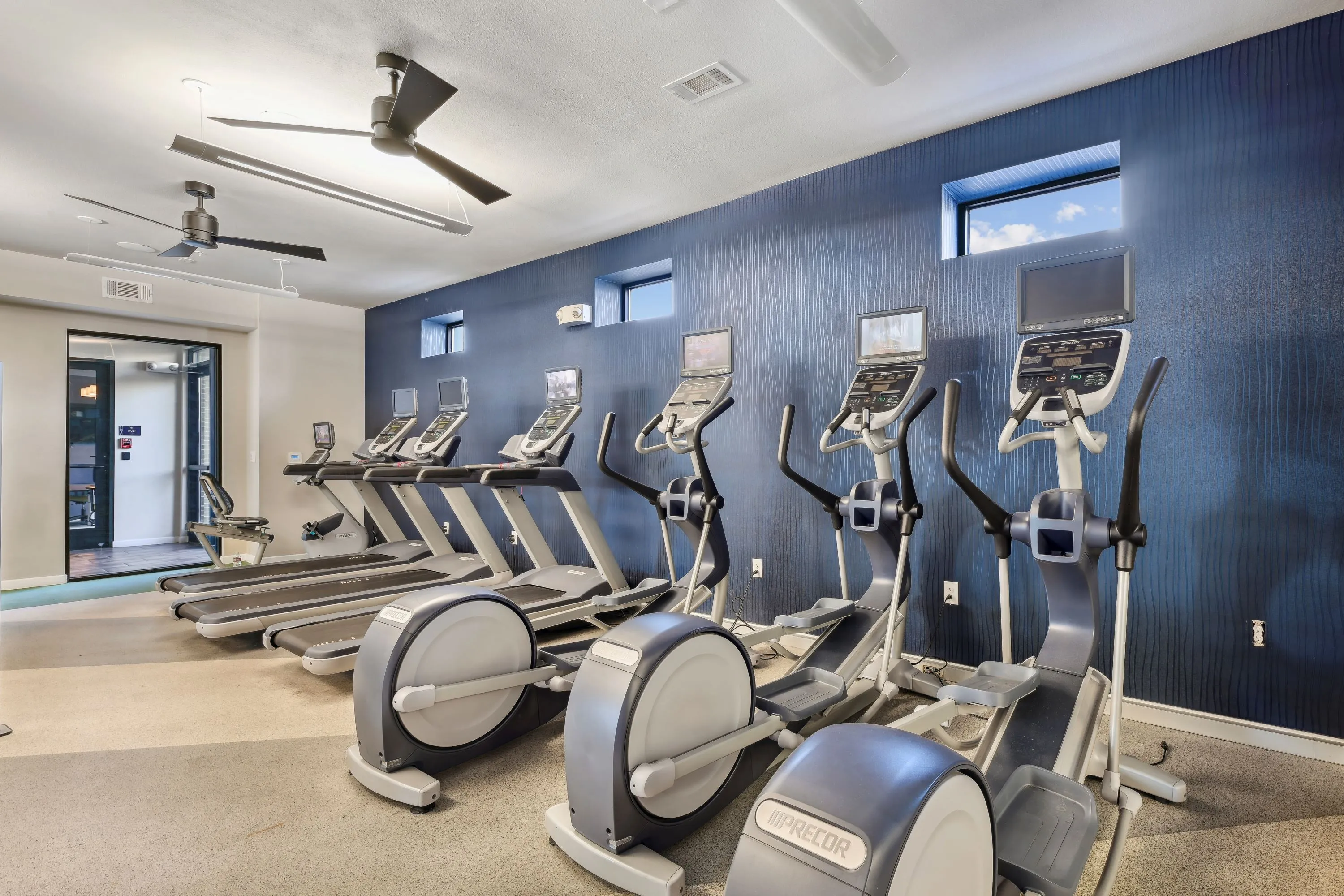 Spacious fitness center with various cardio machines like treadmills and ellipticals, and a distinctive blue accent wall, available to residents at Altitude in Houston, TX.