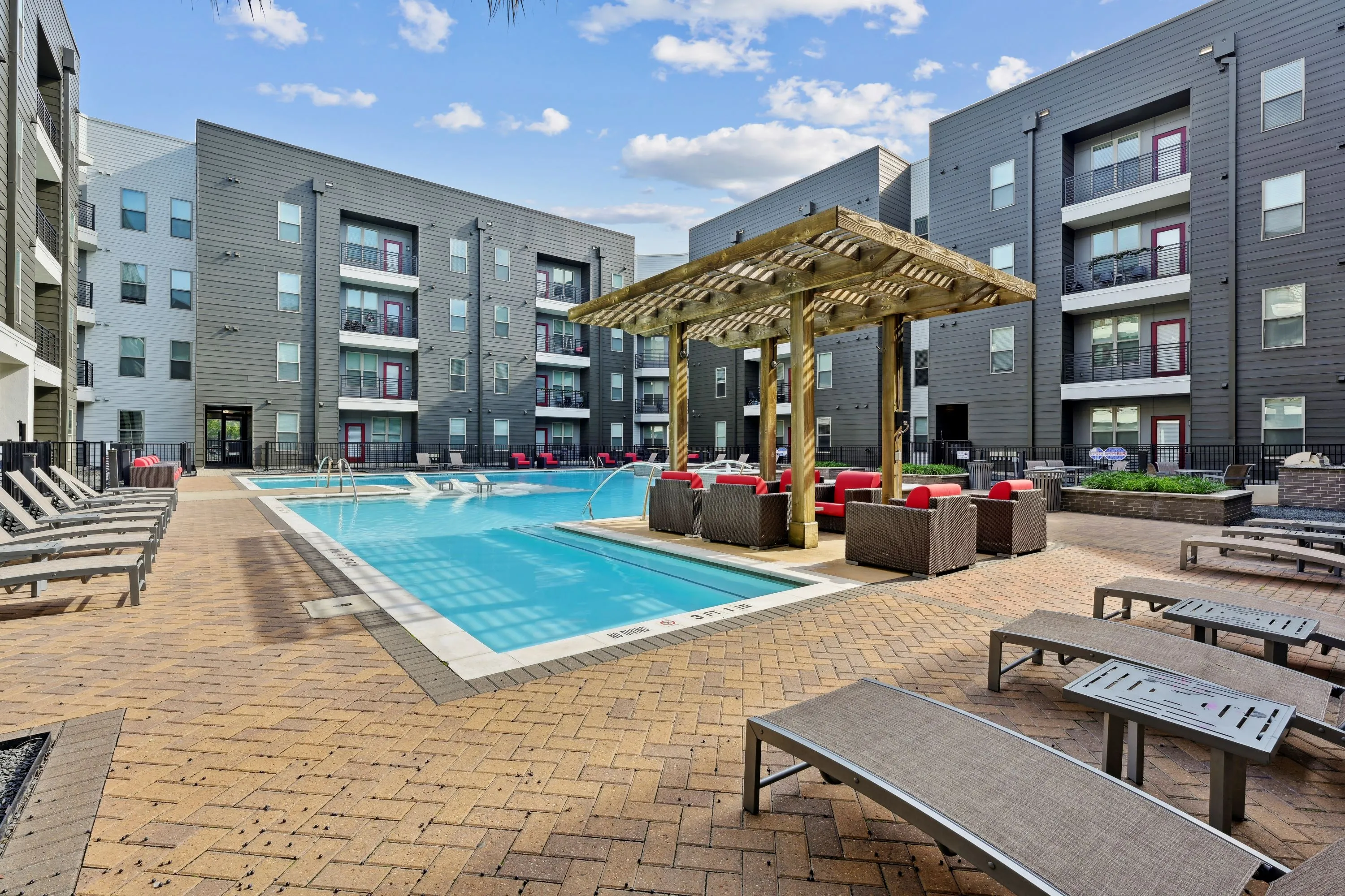 Resort-style swimming pool area with a wooden pergola, lounge chairs, and modern apartment buildings, offering a vibrant outdoor space at Altitude in Houston, TX.