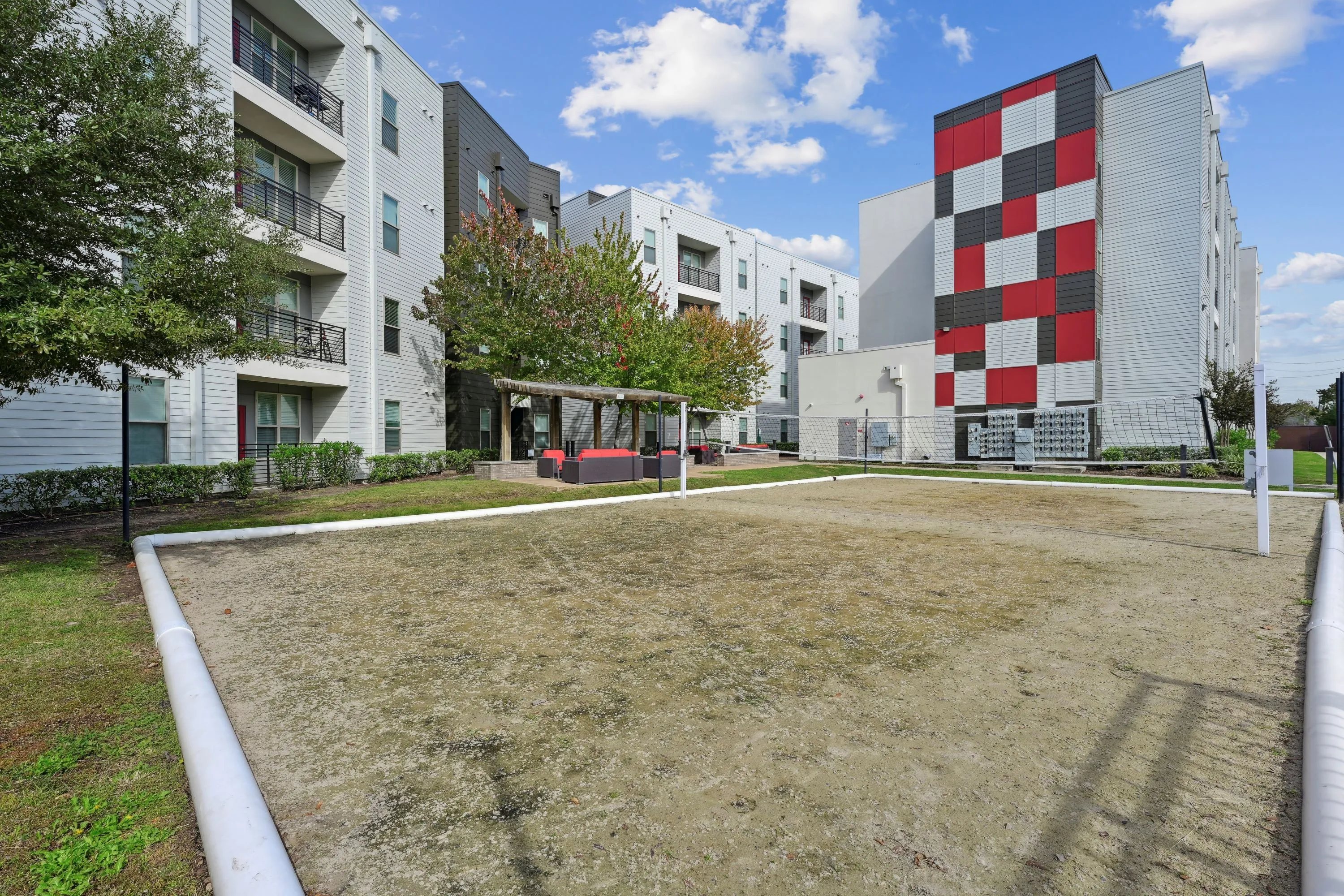 Outdoor sand volleyball court with apartment buildings and a communal lounge area in the background, providing recreational amenities at Altitude in Houston, TX.