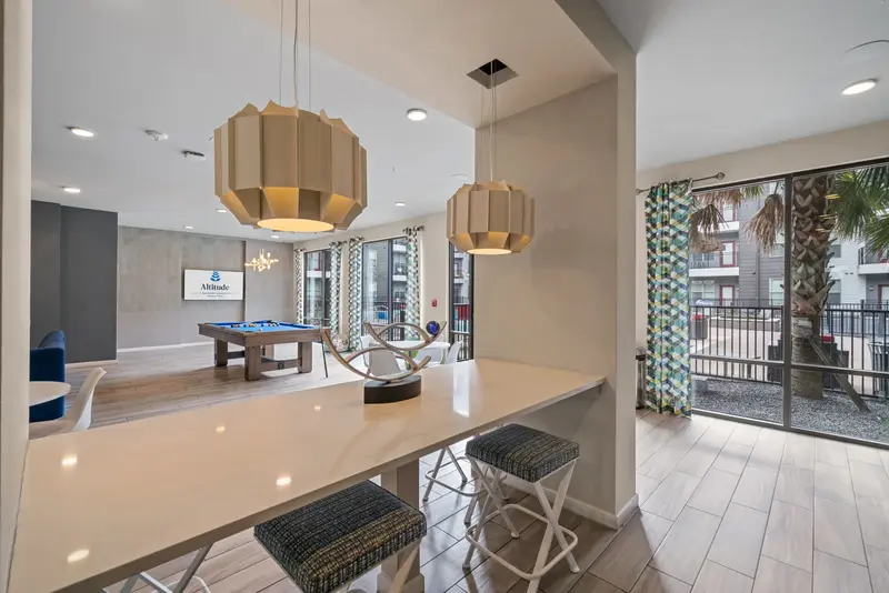Modern resident lounge with a long bar counter, stylish pendant lights, and pool views, offering a chic social space at Altitude in Houston, TX.