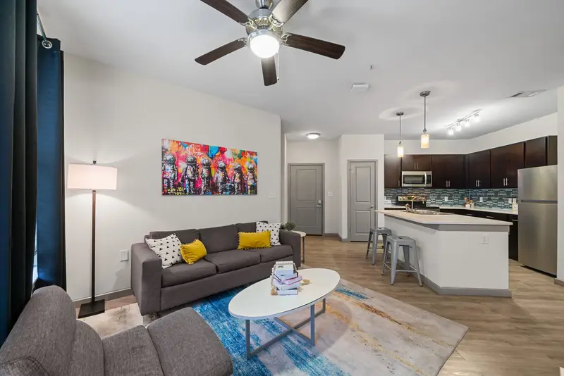 Contemporary living room in an apartment at Altitude in Houston, TX, featuring a grey sofa, colorful art, and an open layout connecting to the kitchen.