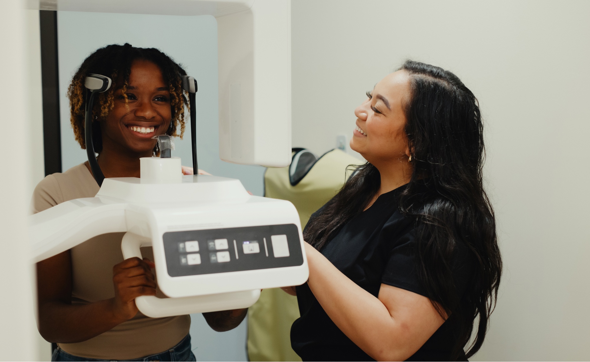 A smiling woman undergoes a dental X-ray while a dentist from Montvale Prosthodontics observes and adjusts the machine.