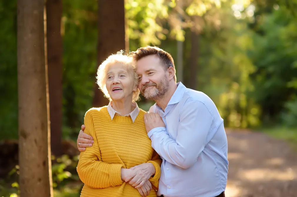 Une mère âgée partage un moment de tendresse avec son fils lors d'une promenade en forêt. Monka valorise ces liens précieux en accompagnant les aidants dans leur rôle au quotidien.