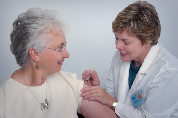 Une patiente âgée souriante reçoit une injection dans le bras d'une infirmière en blouse blanche.