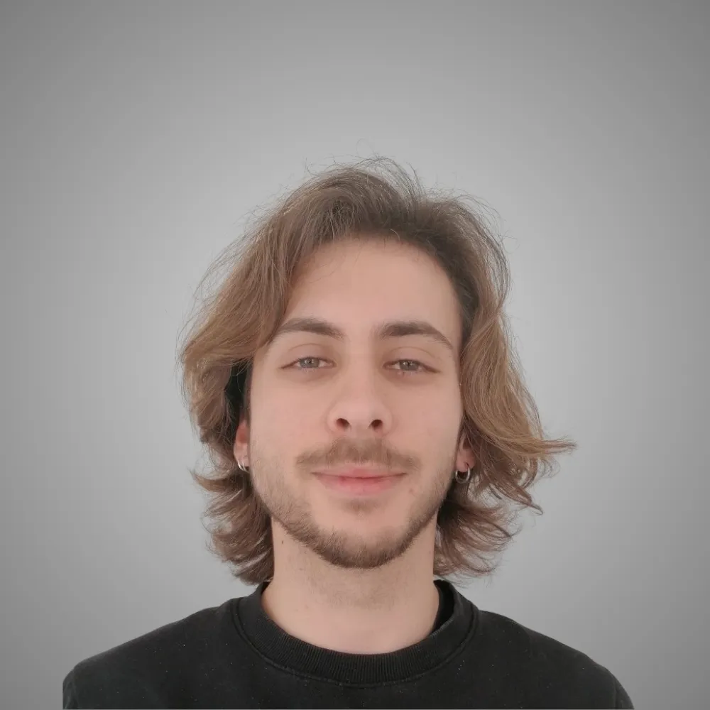 Portrait d'un jeune homme souriant avec cheveux mi-longs et bouclés, portant un sweat noir.