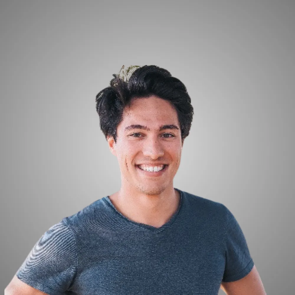 Jeune homme souriant portant un t-shirt bleu sur un fond gris uni.
