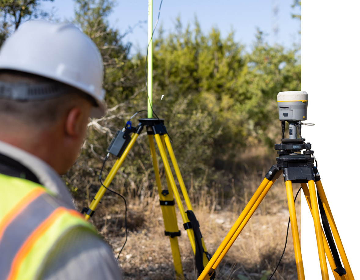 Surveyor in a hard hat and safety vest working with yellow tripods and surveying equipment in outdoors.