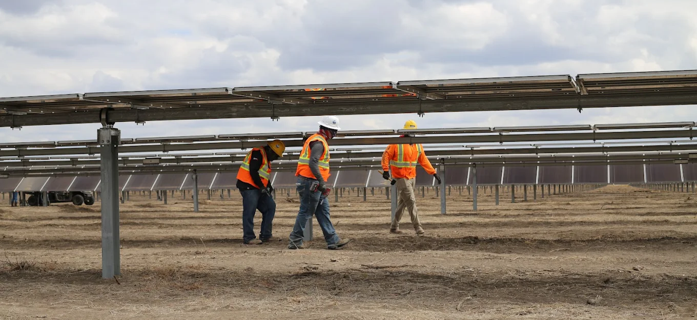 Construction workers survey solar panel installation site with safety equipment