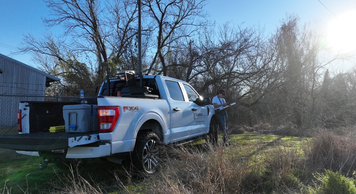 Professional surveyor with survey equipment and blue pickup truck in rural field