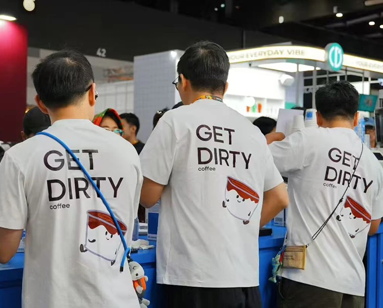 Three smiling people with event badges posing and making peace signs at a booth with Milk branding.