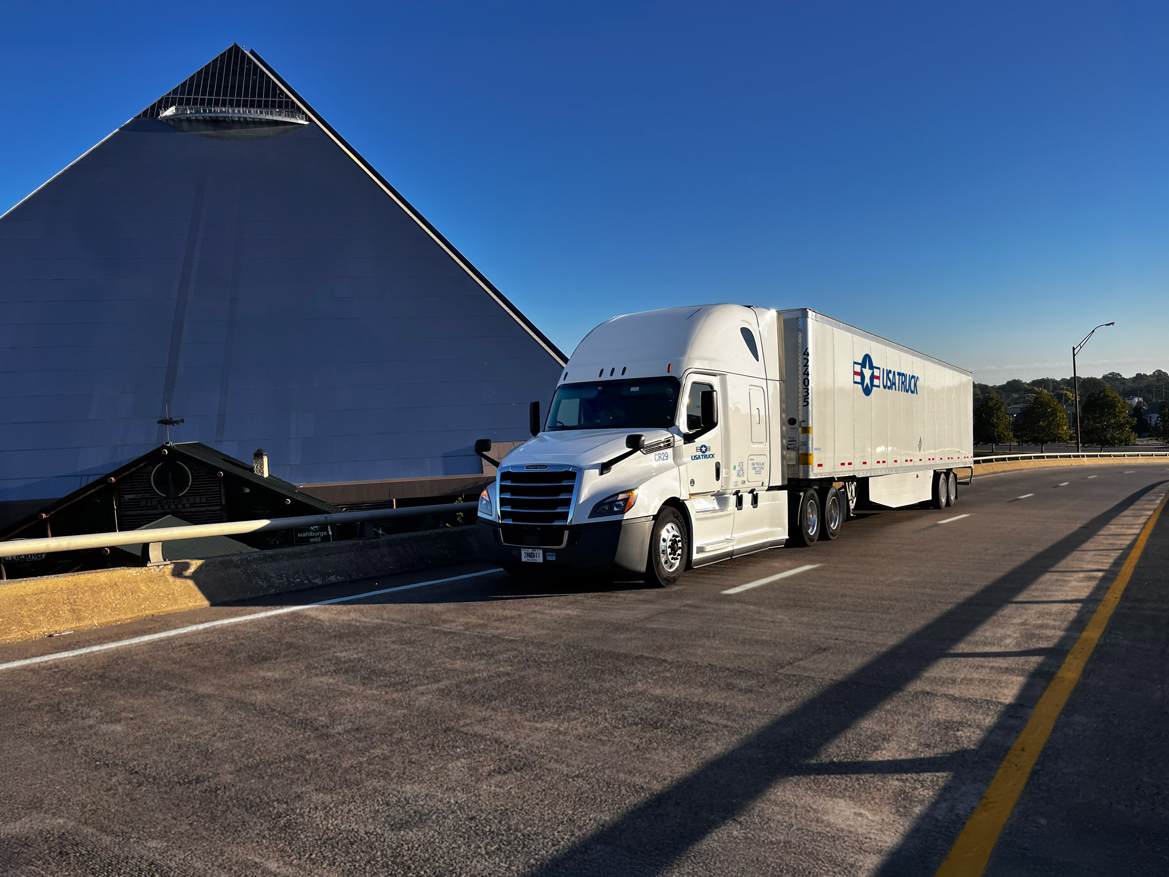 semi truck driving down the road in front of a large pyramid shaped building