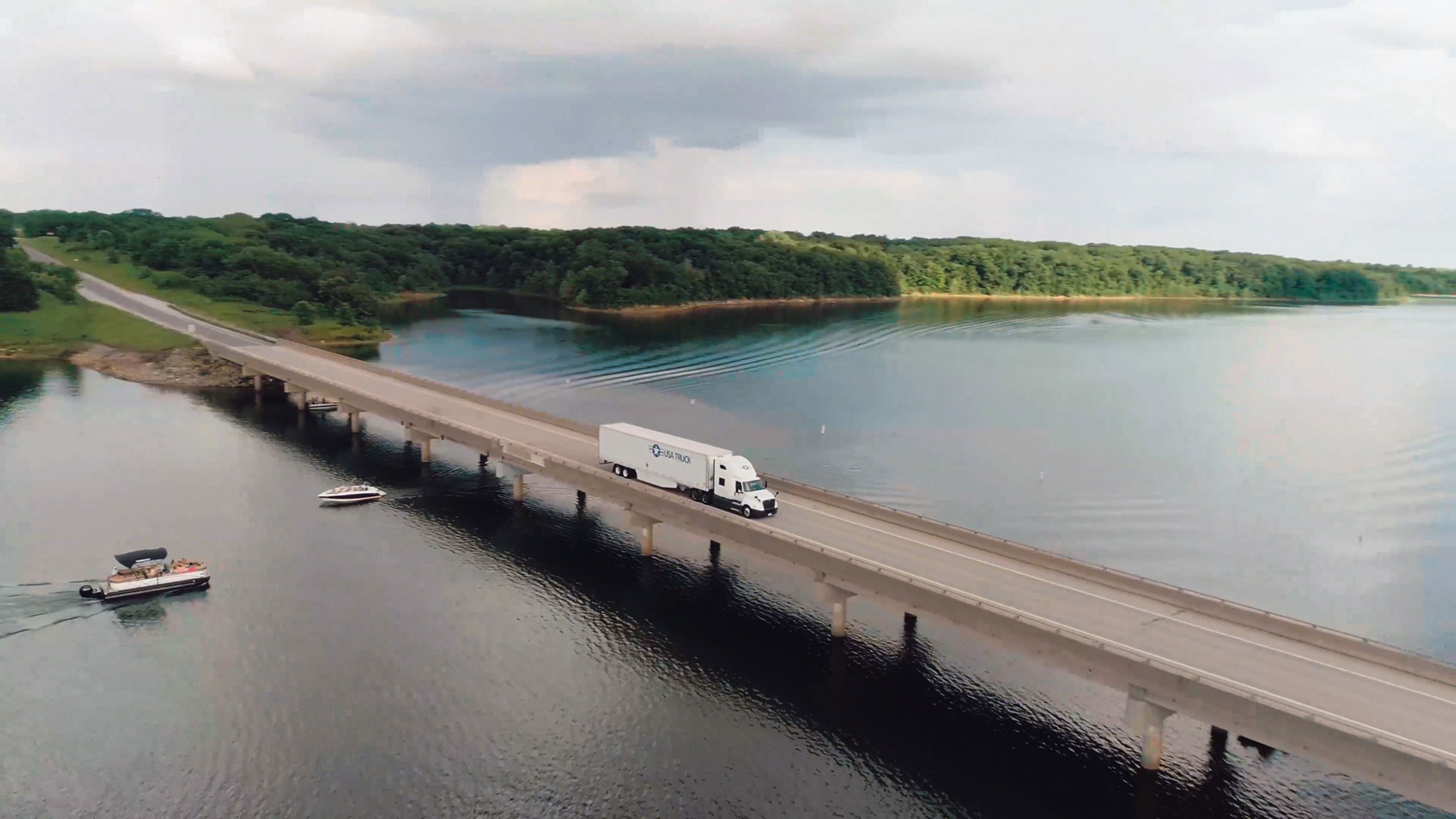 semi truck driving down the road over bridge with lake