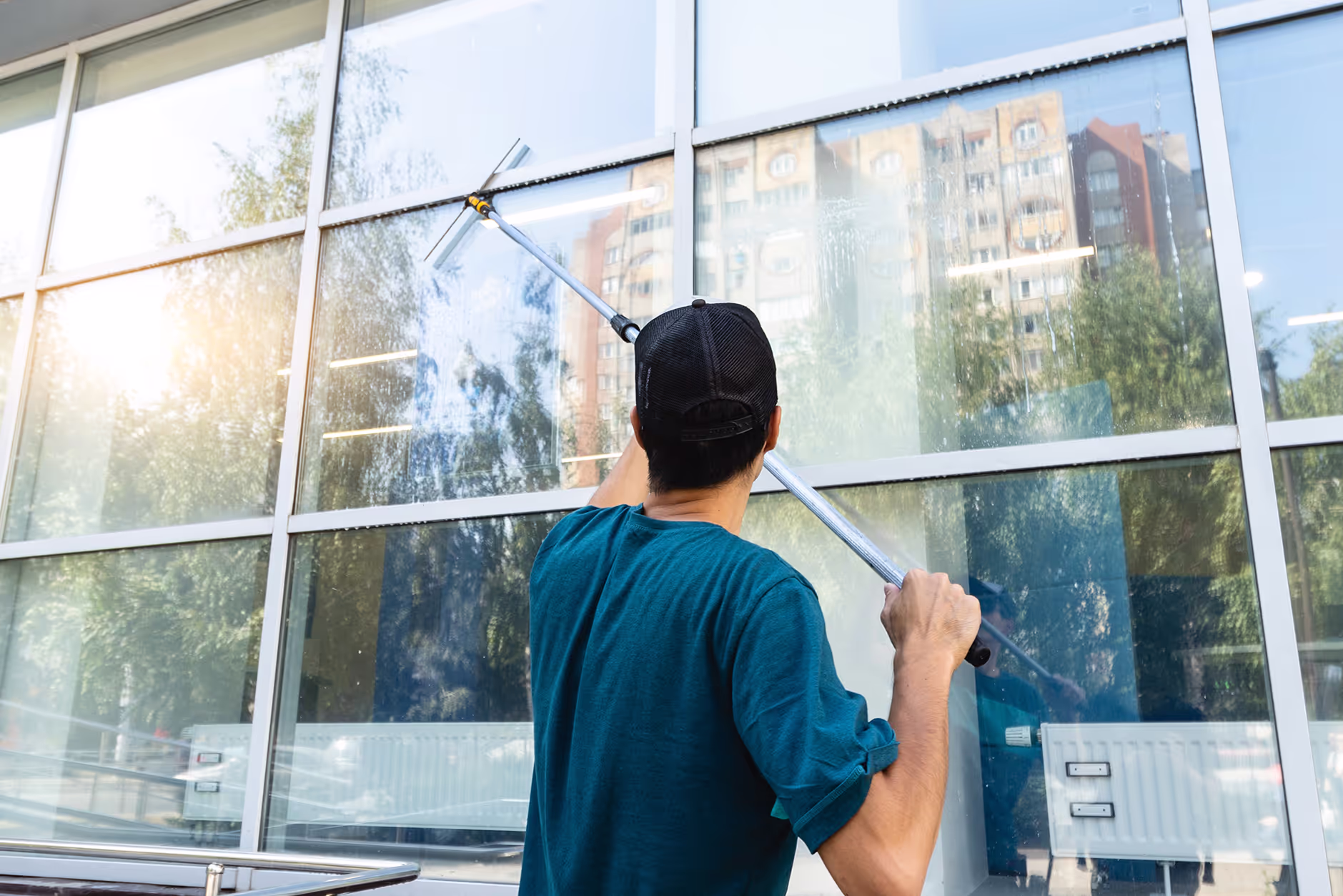 A professional cleaner using a squeegee to clean large residential windows on a sunny day.