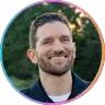 Smiling man outdoors with short brown hair and trimmed beard.