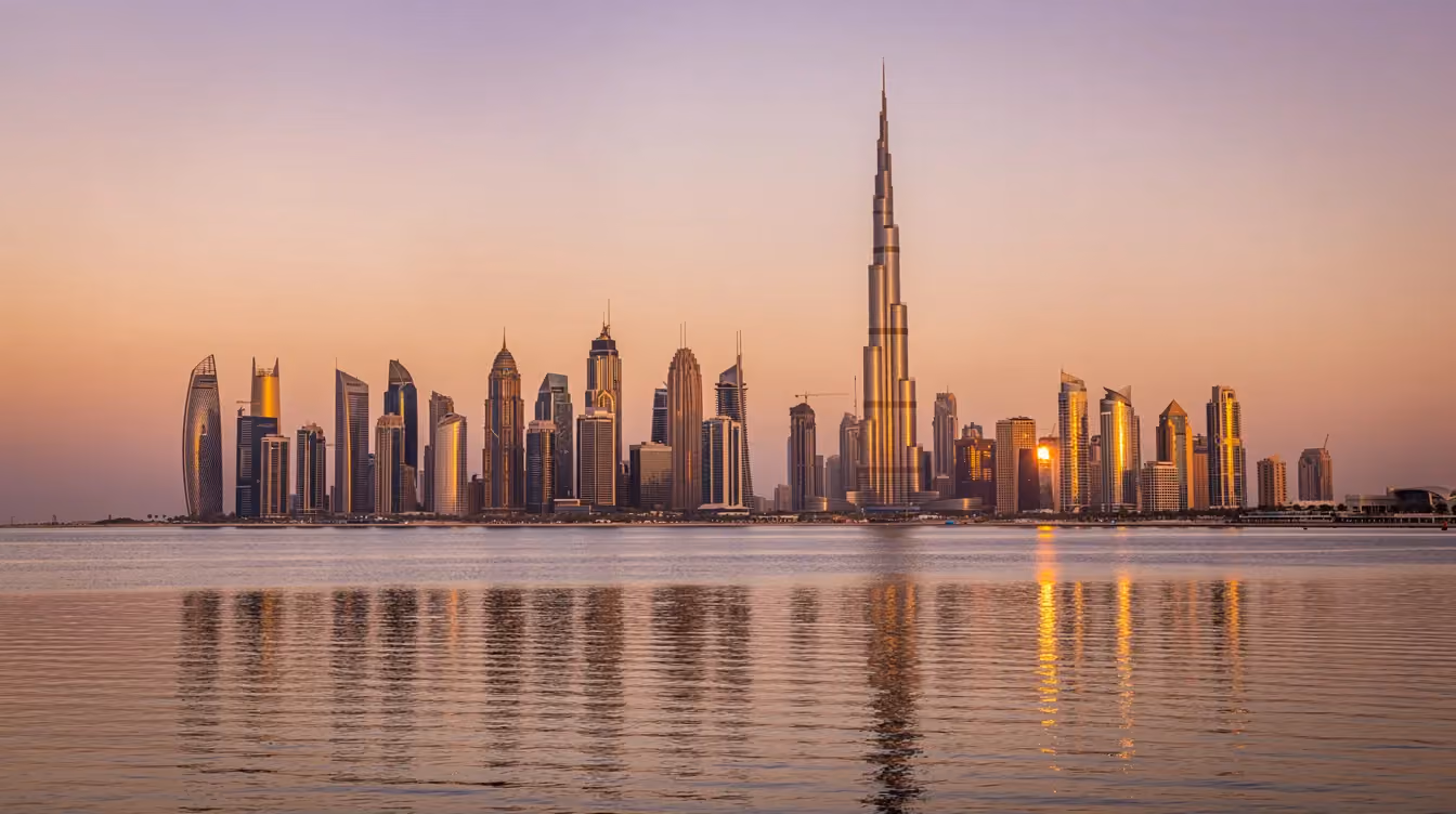 Das Panorama der Skyline von Dubai bei Sonnenuntergang zeigt beeindruckende Wolkenkratzer, die sich über das Wasser erstrecken, während die Farben des Himmels in warmen Tönen leuchten. Im Hintergrund ist die berühmte Palm Jumeirah zu sehen, ein Symbol für Luxusimmobilien in den Vereinigten Arabischen Emiraten.