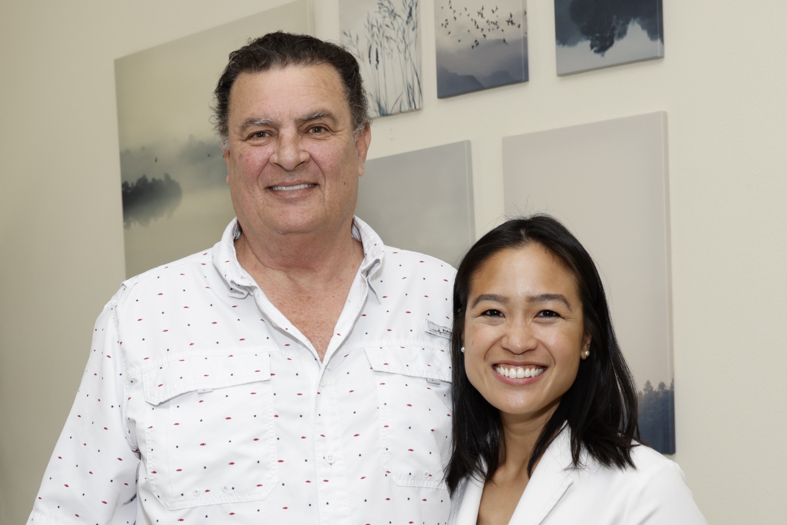 Woman doctor in white coat shows dental X-ray with implants on a screen to smiling man.