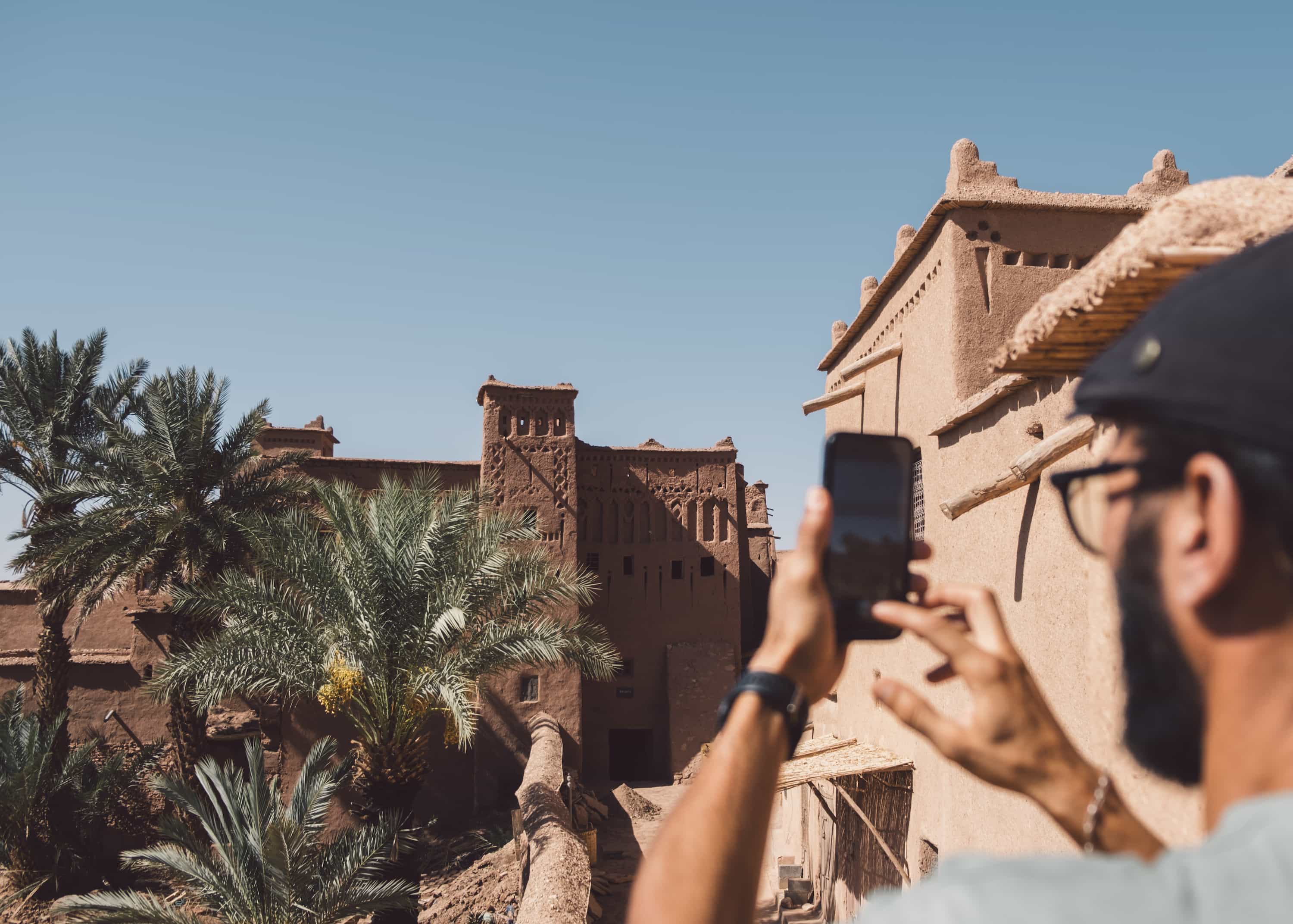 A traveler photographing the ancient kasbah of Aït Ben Haddou on a phone