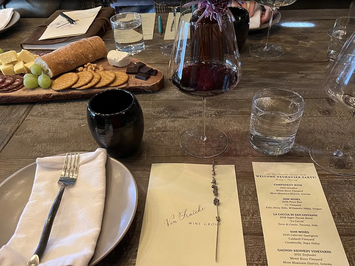A rustic table set for a wine tasting event in Napa Valley, featuring a cheese and charcuterie board, wine glasses, a menu, and a carafe of red wine.