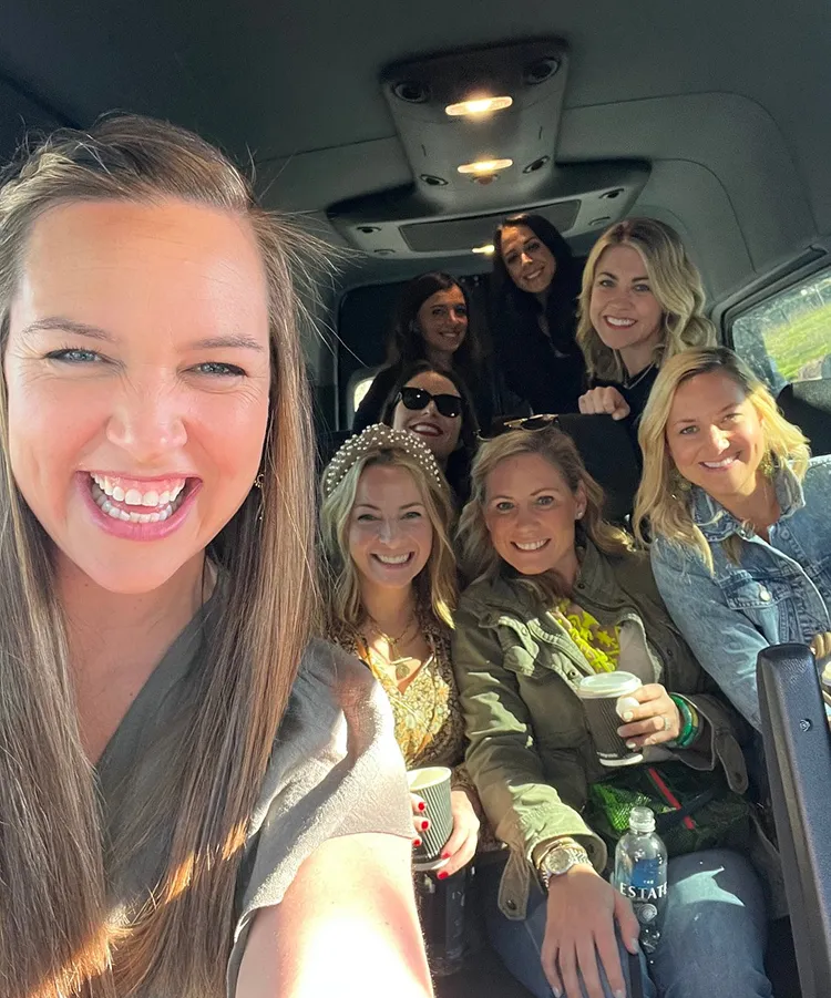 A group of women taking a selfie inside a van, smiling and holding drinks, during a trip through Napa Valley.