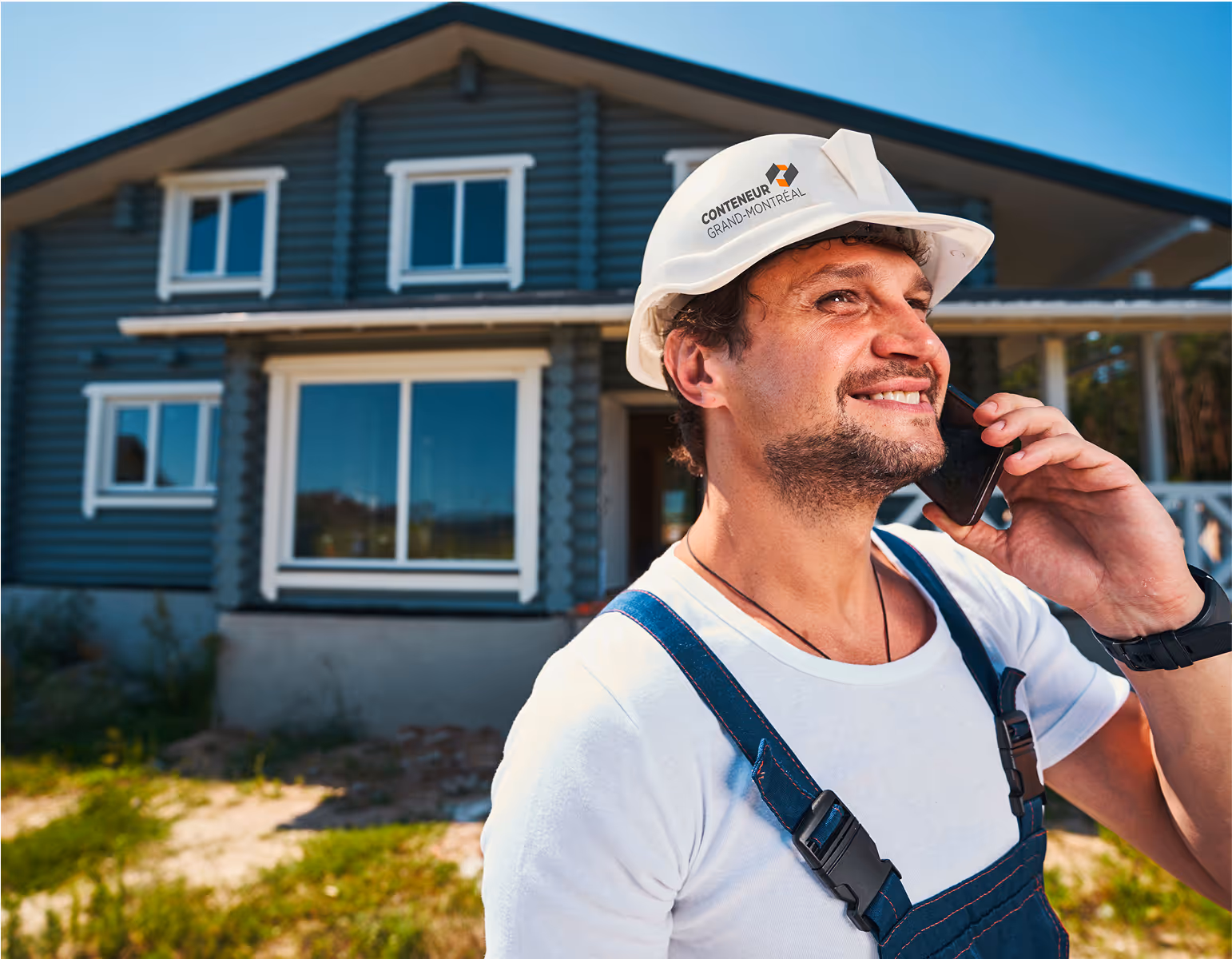 Ouvrier souriant au téléphone devant une maison en bois bleu