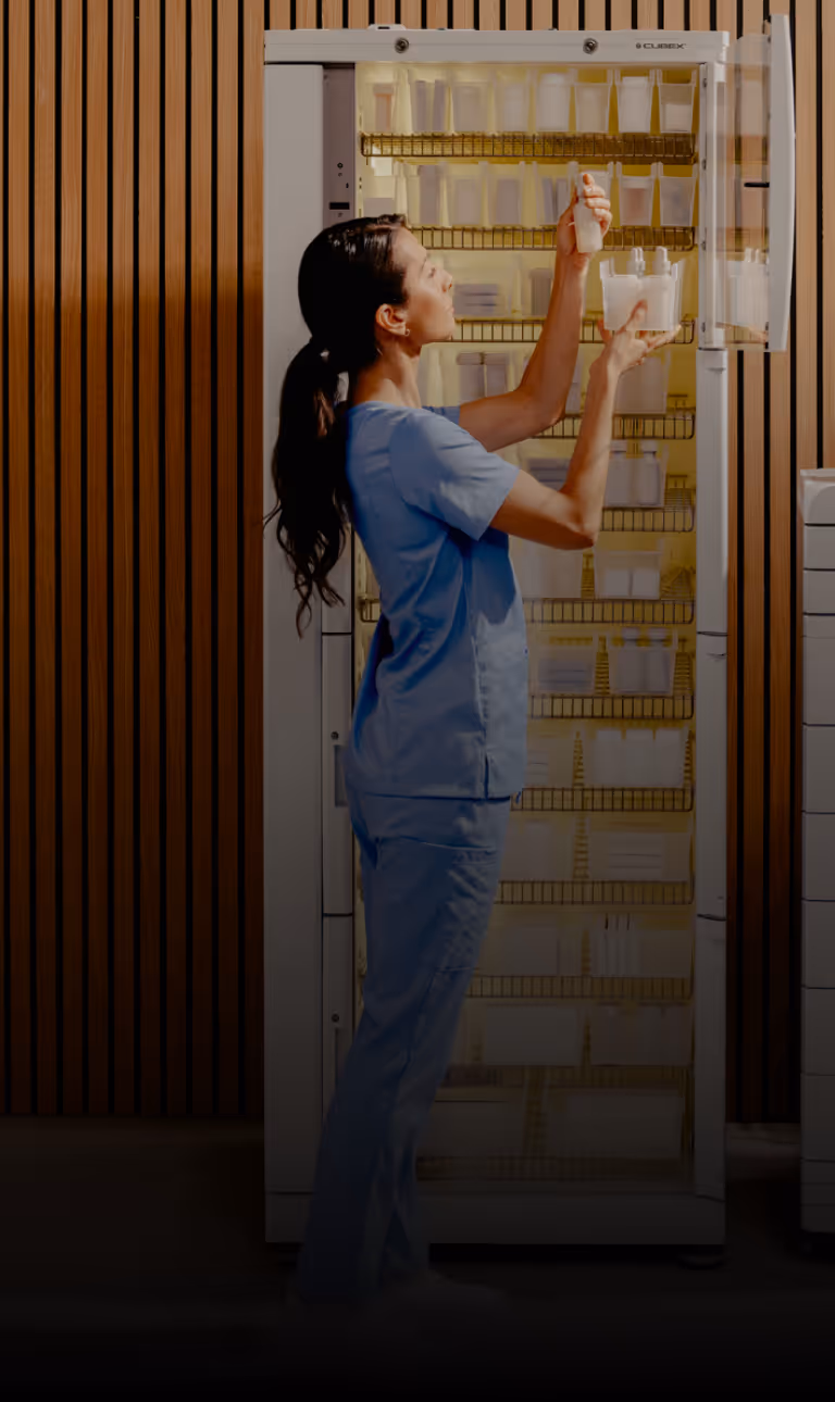 Medical professional in blue scrubs organizing medical supplies in a CUBEX cabinet.