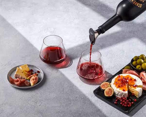 Commercial photography of red wine pouring into glasses, styled with cheese, figs, and olives.