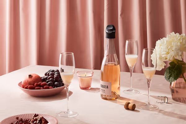 Beverage photography featuring a blush-toned dinner party scene with sparkling wine, champagne flutes, fruit bowl, candlelight, and soft pink backdrop.