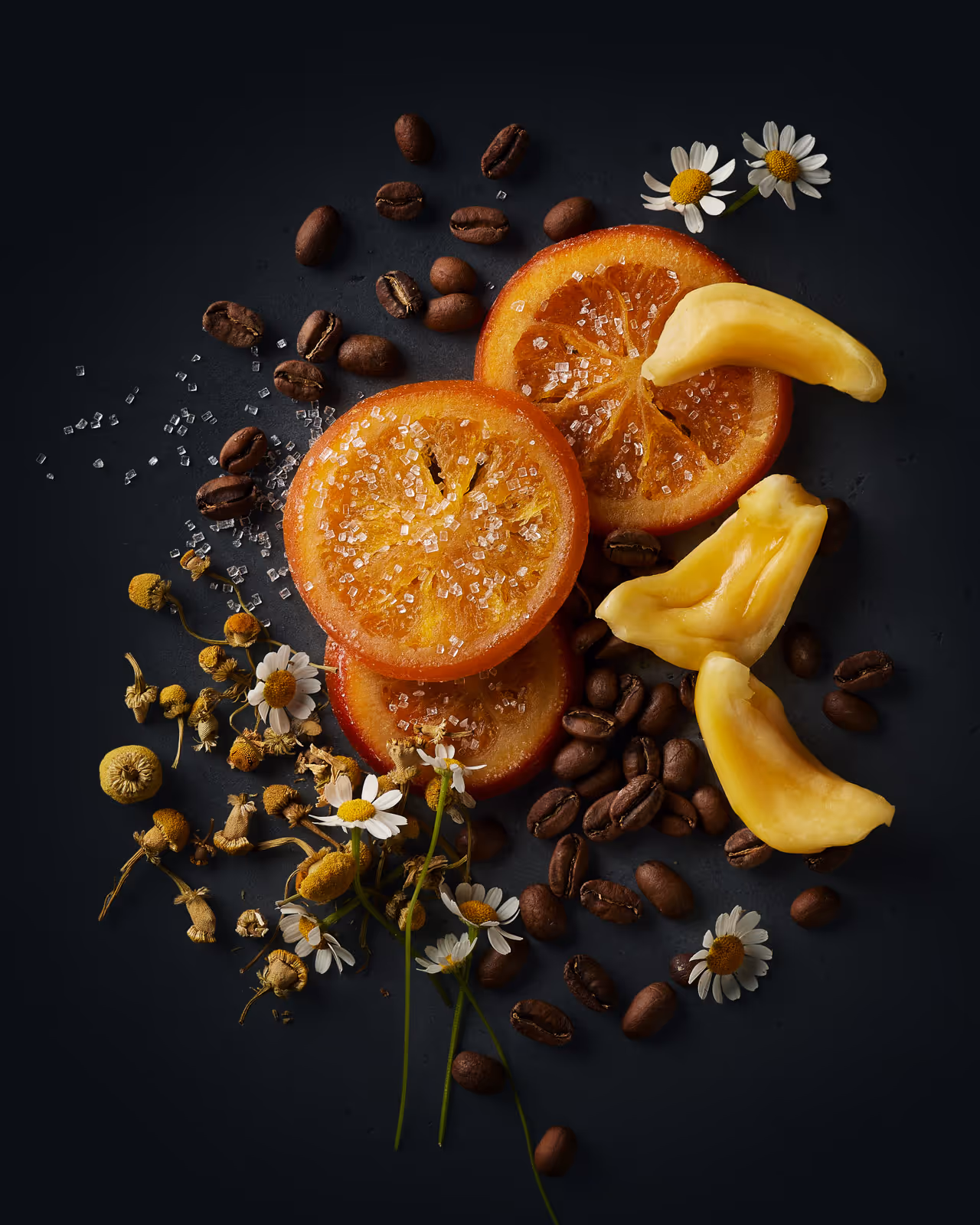 Flat lay of dried orange slices, coffee beans, white flowers, and jackfruit chunks on a dark background. Styled flavor profile by Phoenix, Arizona food photographer.