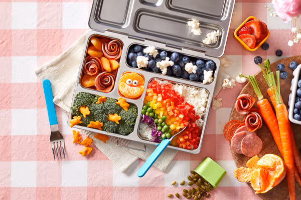 Top-down view of a colorful children's lunchbox meal, creating a vibrant spring. Image showcases nutritious and visually appealing meal prep options for kids, perfect for school lunches or picnics in the sunny weather.