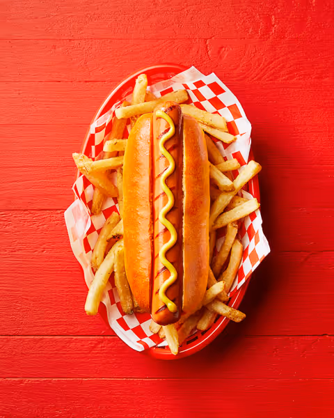 Classic hot dog with fries food photography styled on a vibrant red background.