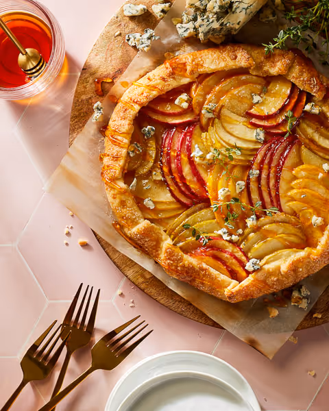Styled food photography, featuring a baked apple galette on a blush tile surface