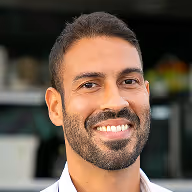 Lachende man met kort haar en baard, zittend in een modern kantoor.