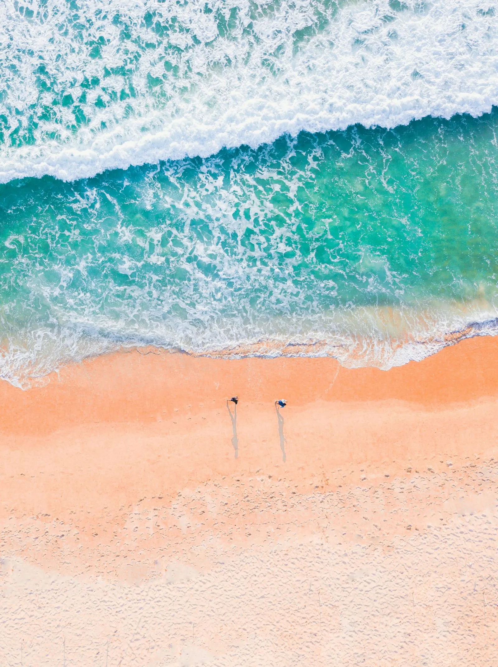 Two people standing on a beach next to the ocean.