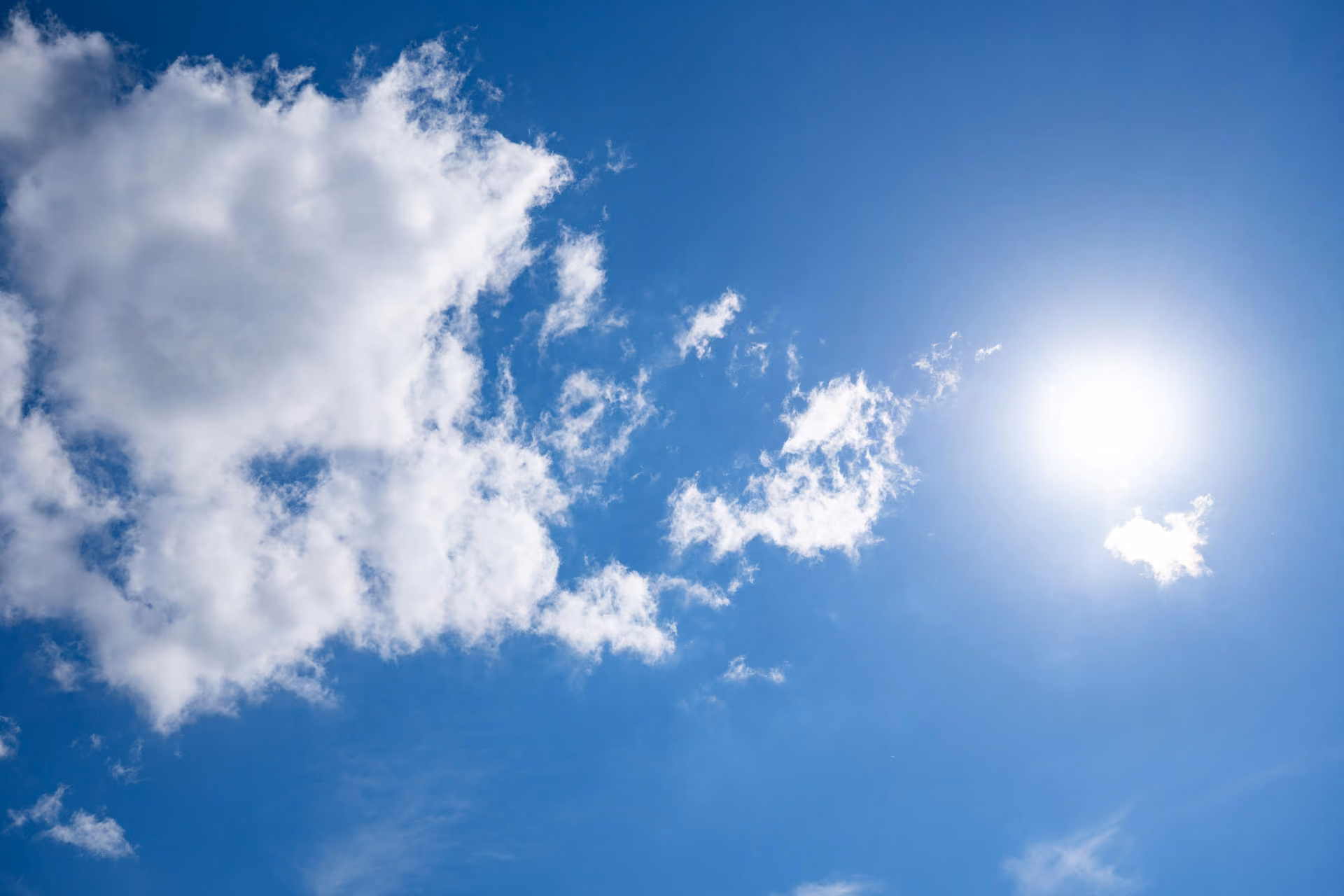 Ciel bleu avec quelques nuages blancs épars et le soleil brillant à droite.