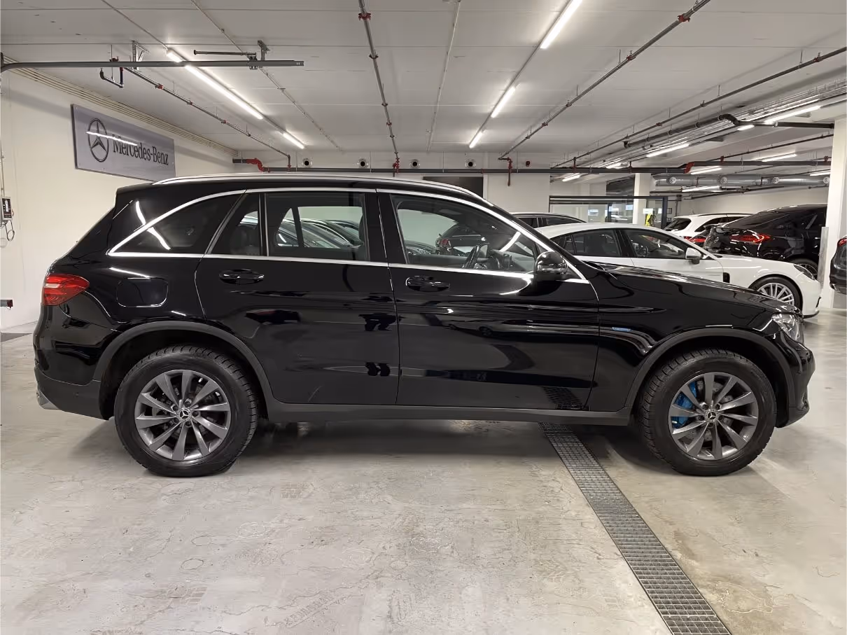 Black Mercedes-Benz SUV parked indoors in a showroom with other cars in the background.