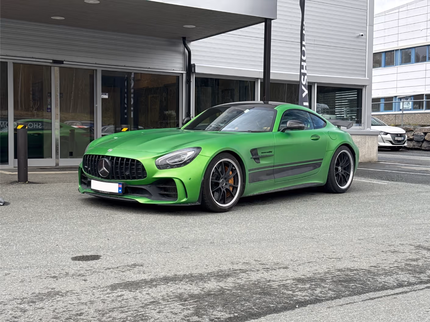 Green Mercedes-AMG GT sports car parked in front of a modern building.