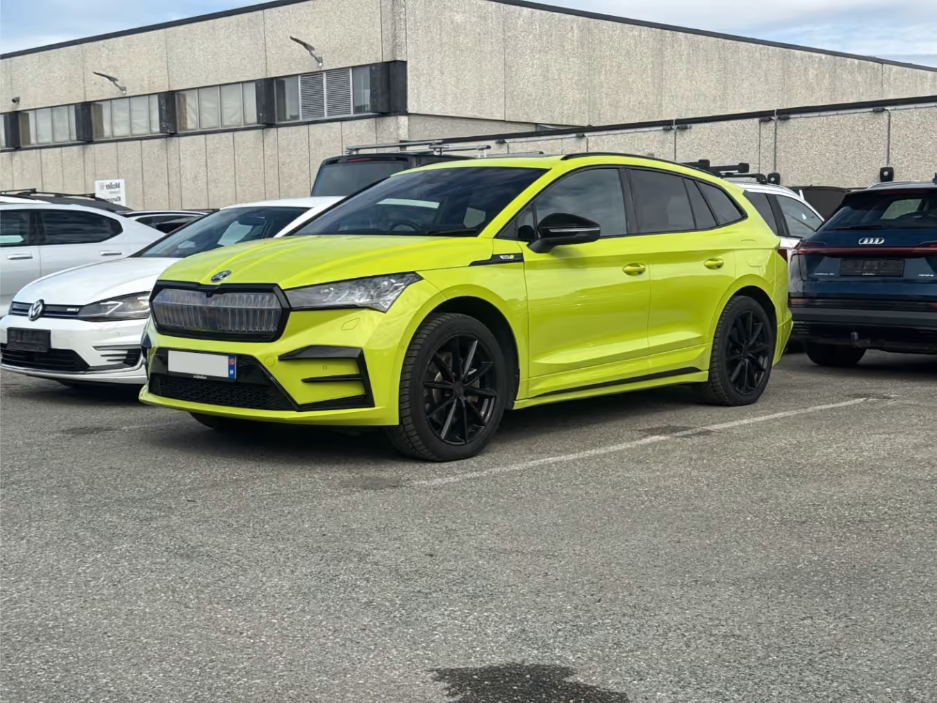 Bright yellow-green Škoda Enyaq parked in front of a commercial building, surrounded by other cars.