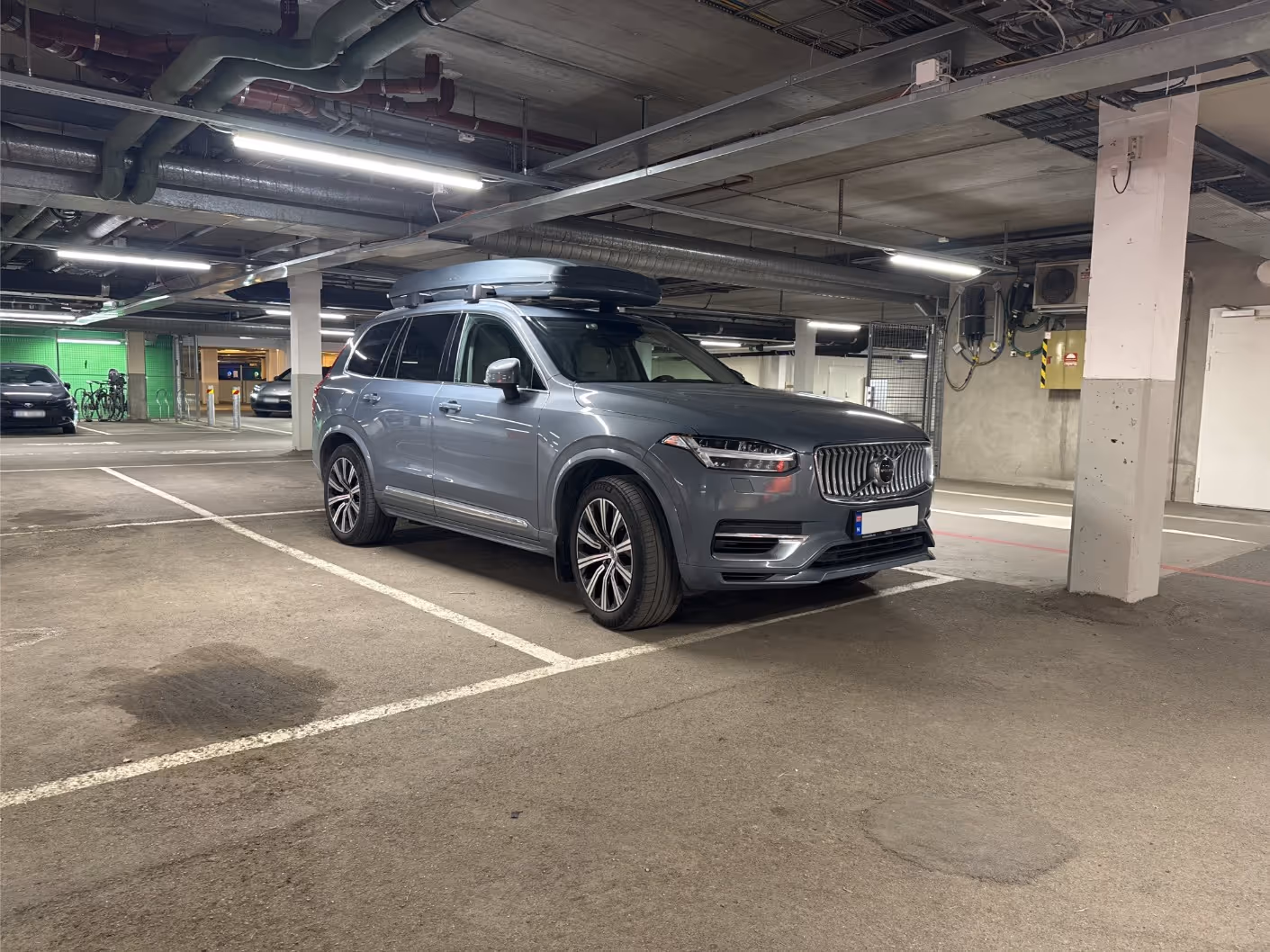 Gray Volvo SUV with roof cargo box parked in an indoor parking garage.