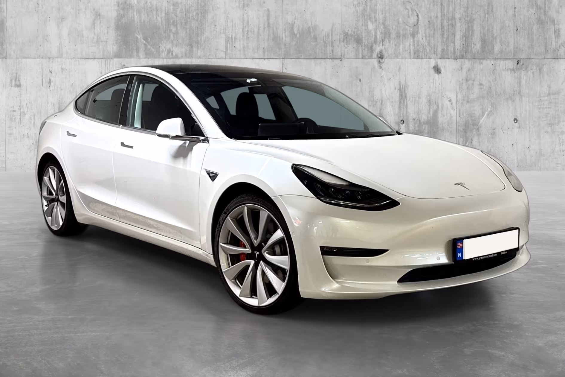 White Tesla Model 3 electric car parked indoors with concrete wall background.
